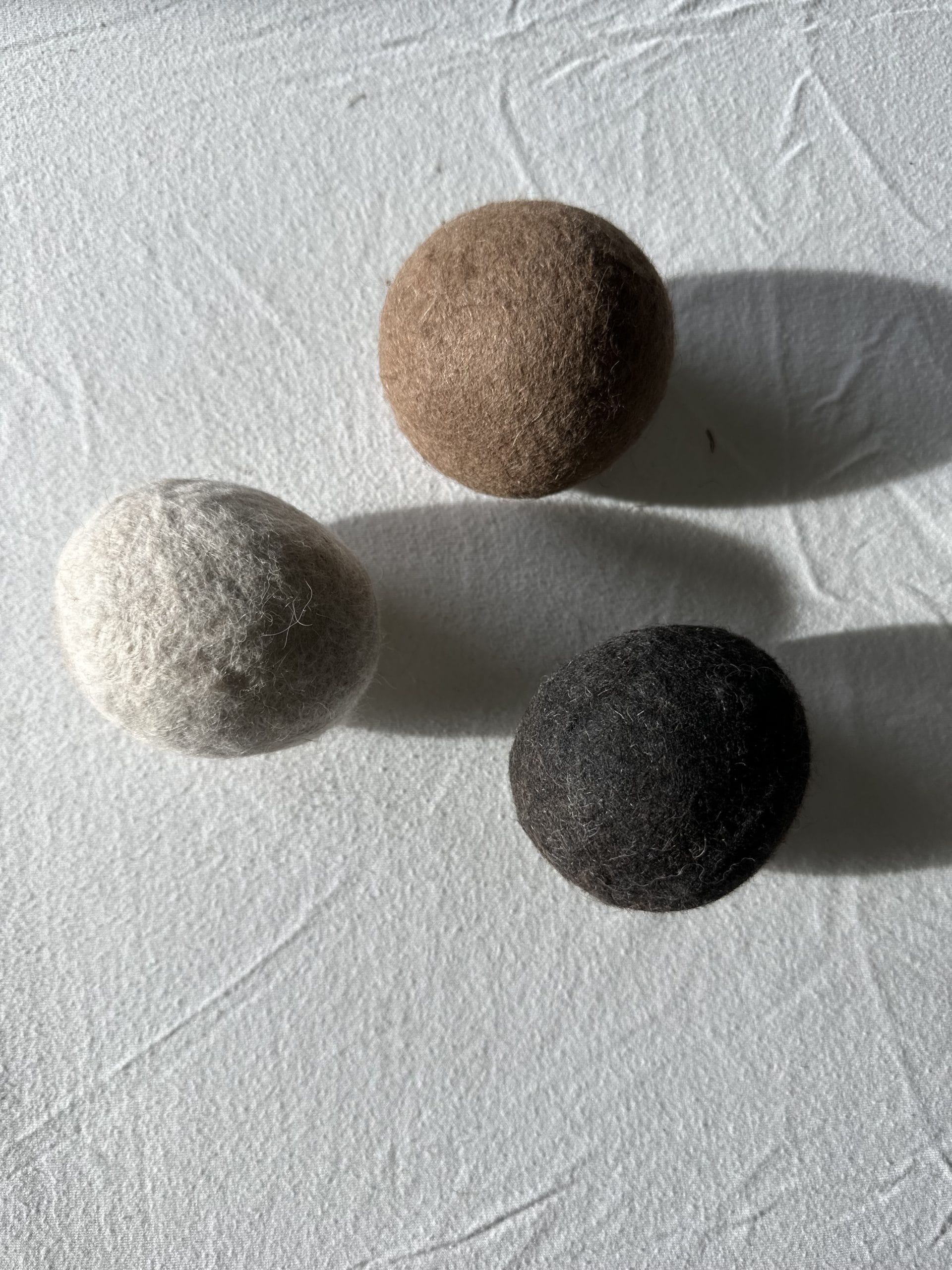 Three Felted Dryer Balls on a white surface.