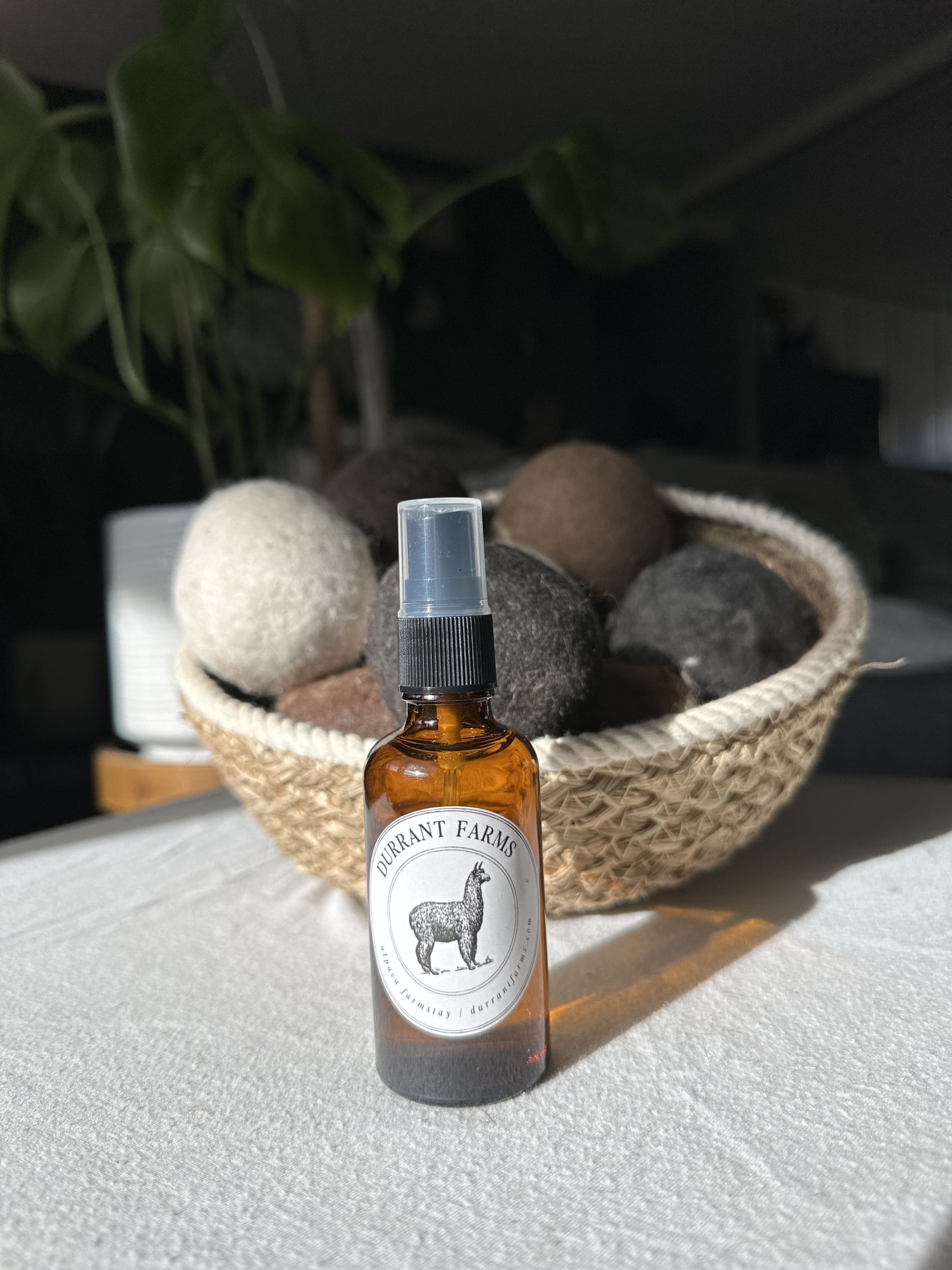 A bottle of Dryer Ball Spray on a table next to a basket.