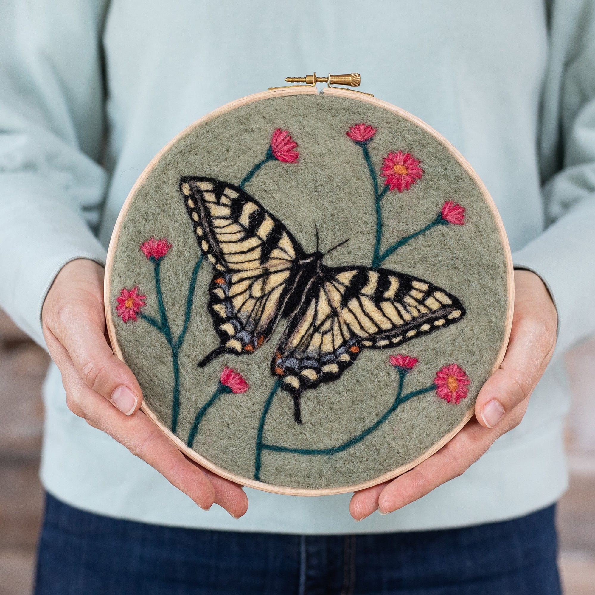 A woman is holding a hoop with a Butterfly Needle Felting Kit on it.