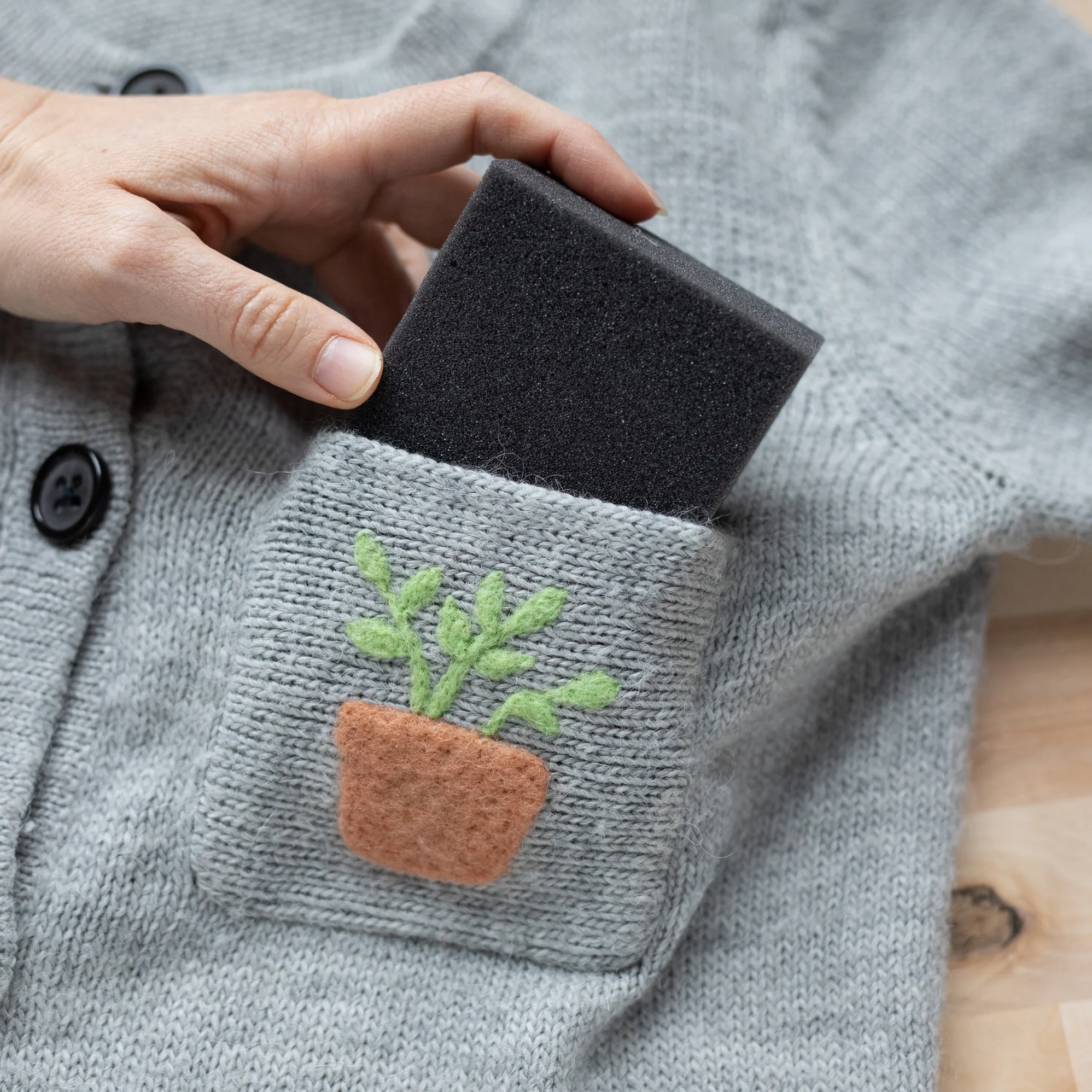 A person holding a 3x3 Foam Mending Mats - set of 4 in a pocket of a sweater.