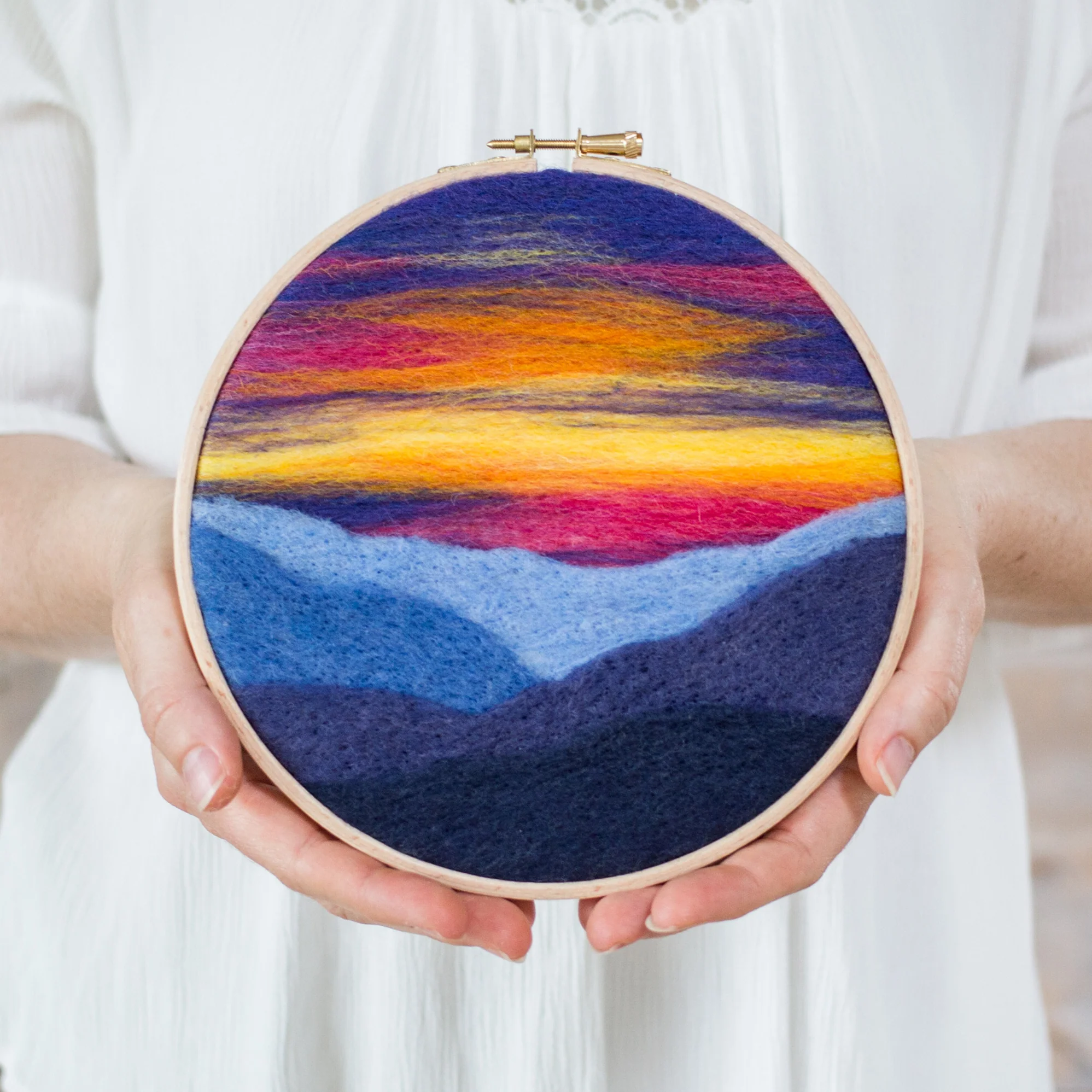 A woman is holding a Mountain Sunset Needle Felting Kit.